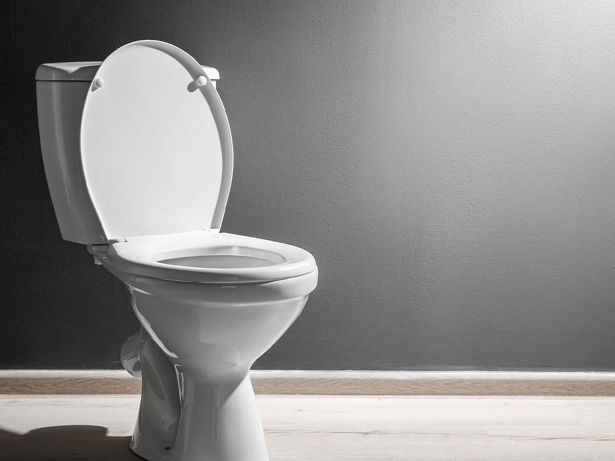 New ceramic toilet bowl near a grey wall.