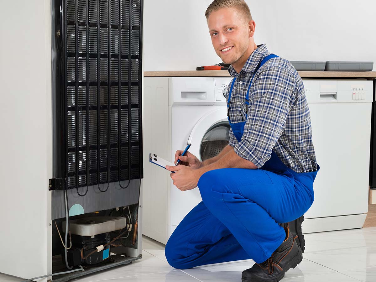 Young Plumber Writing On Clipboard In Front Of Refrigerator