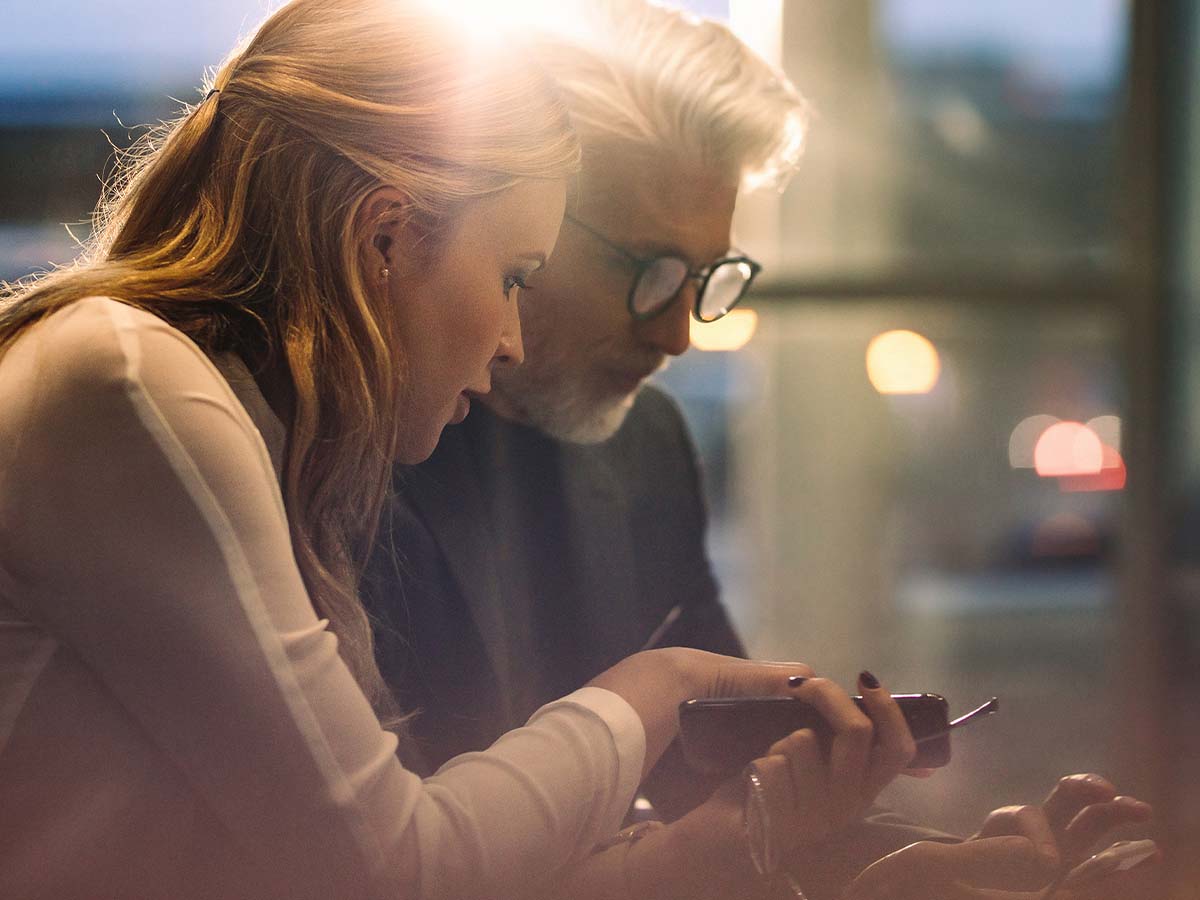 Two people next to each other talking with their phones out in front.