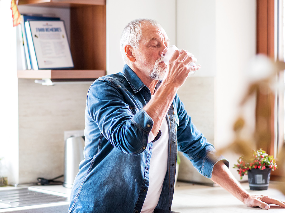 A older gentleman taking a drink from a glass of water