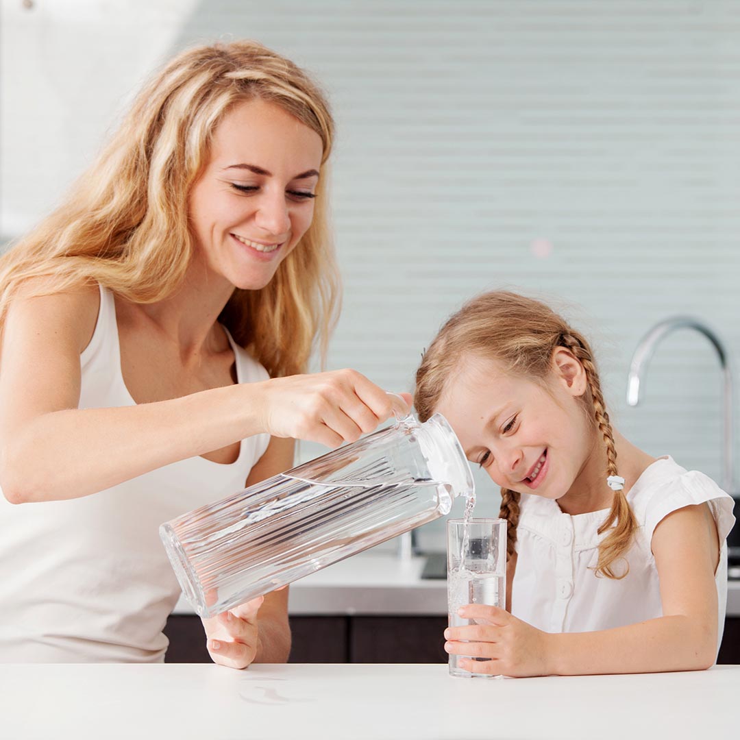 mother pouring a glass of water for her daughter in the kitchen